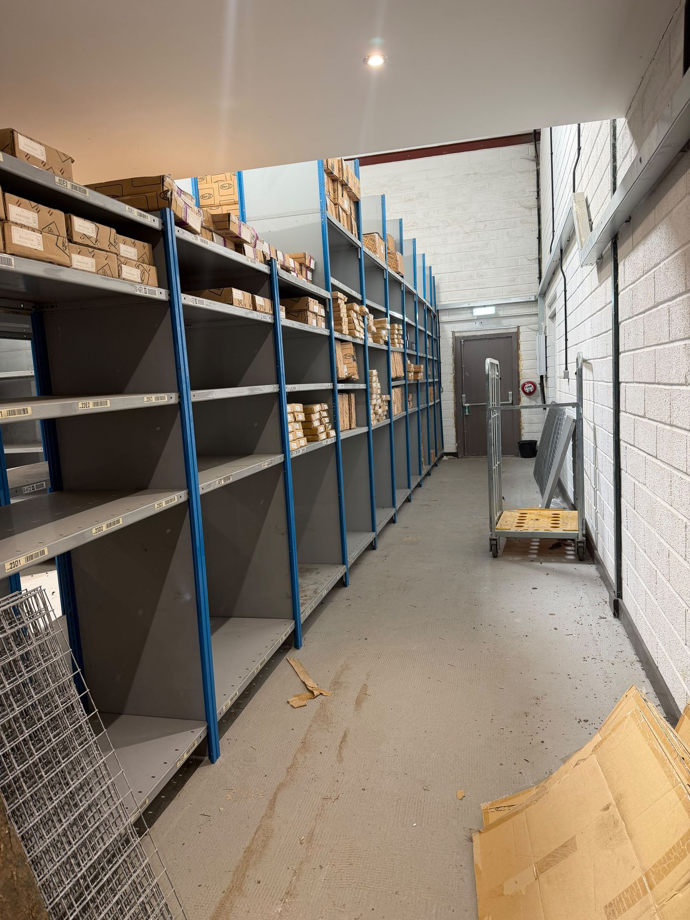Warehouse aisle with shelving, concrete floor and exit door at the rear