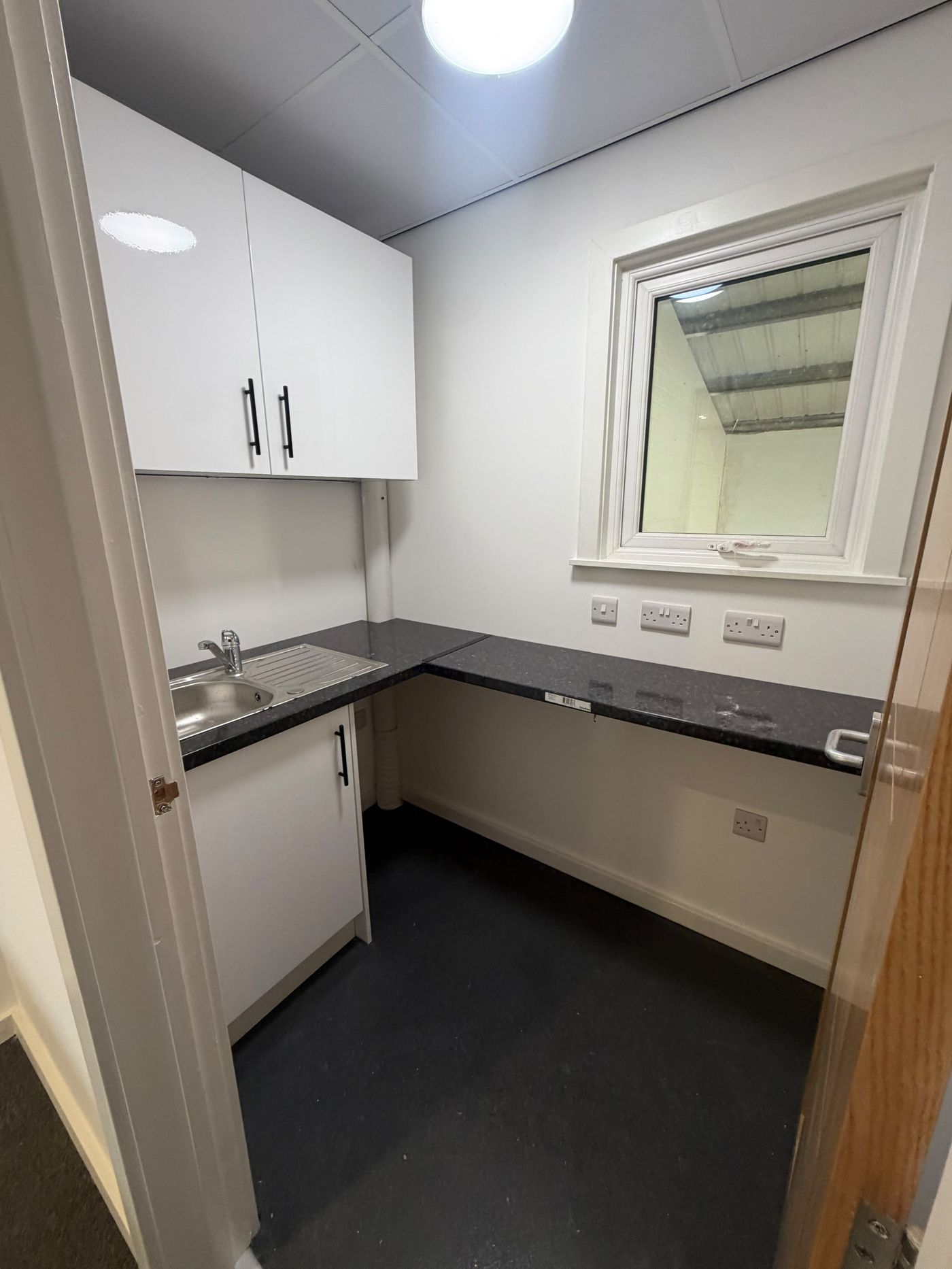 Fitted kitchenette with white units, black worktop and stainless steel sink