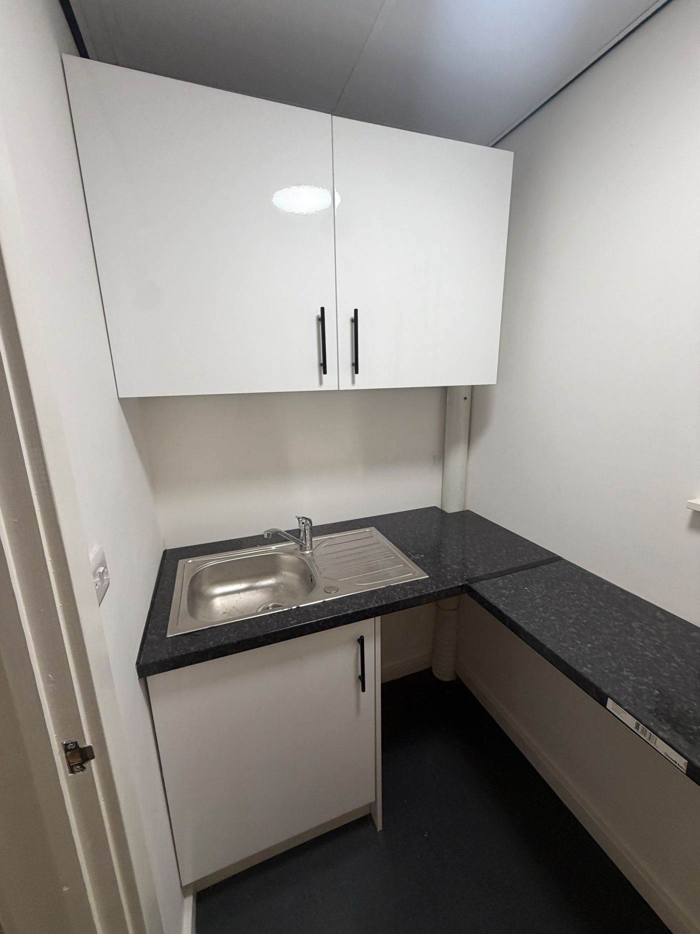 White kitchen units with black speckled worktop and chrome tap